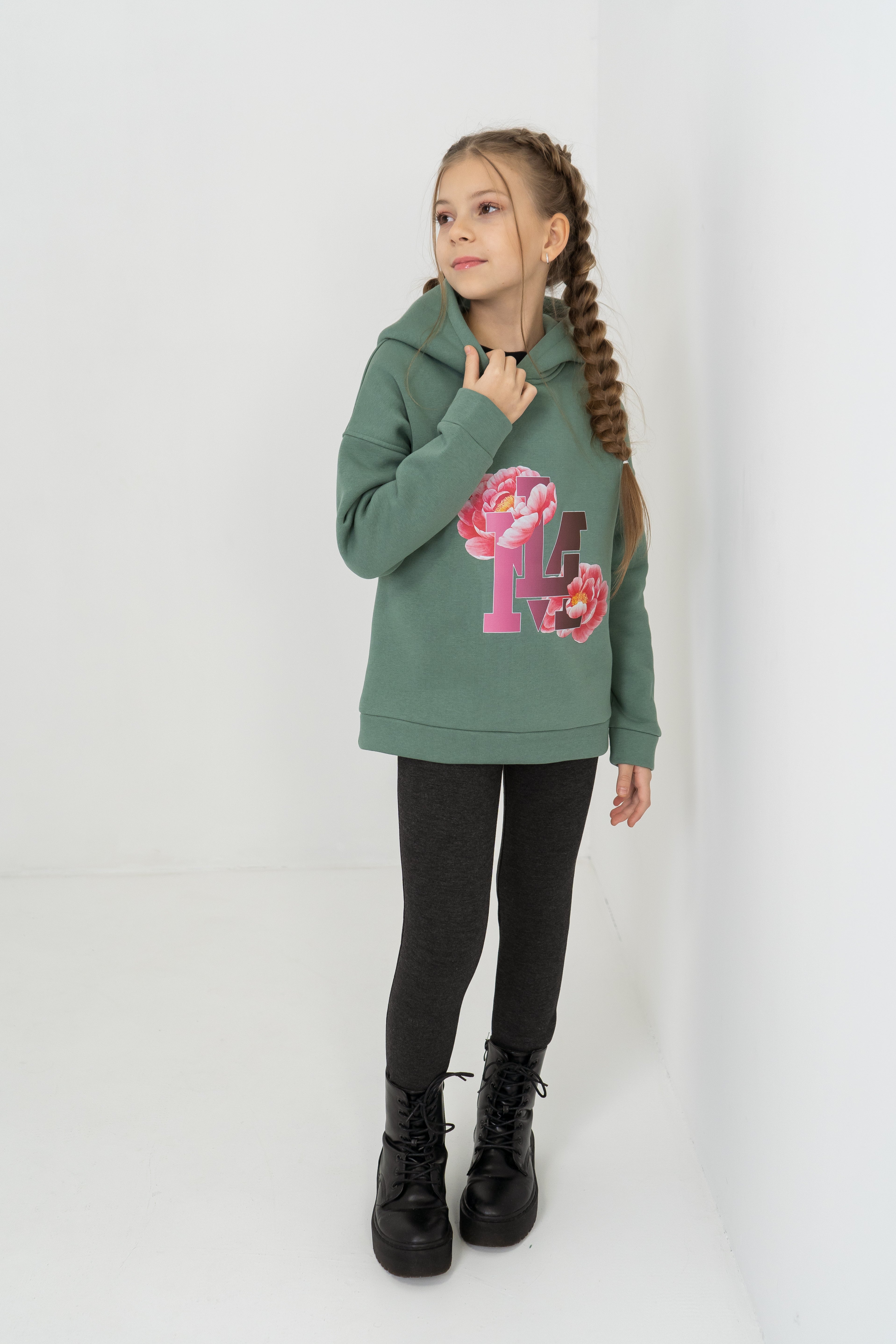 Mädchen hat den komplettern Outfit bei Lemoni Boutique gekauft: grünen Hoodie mit Blumen-Print und graue Thermoleggings.