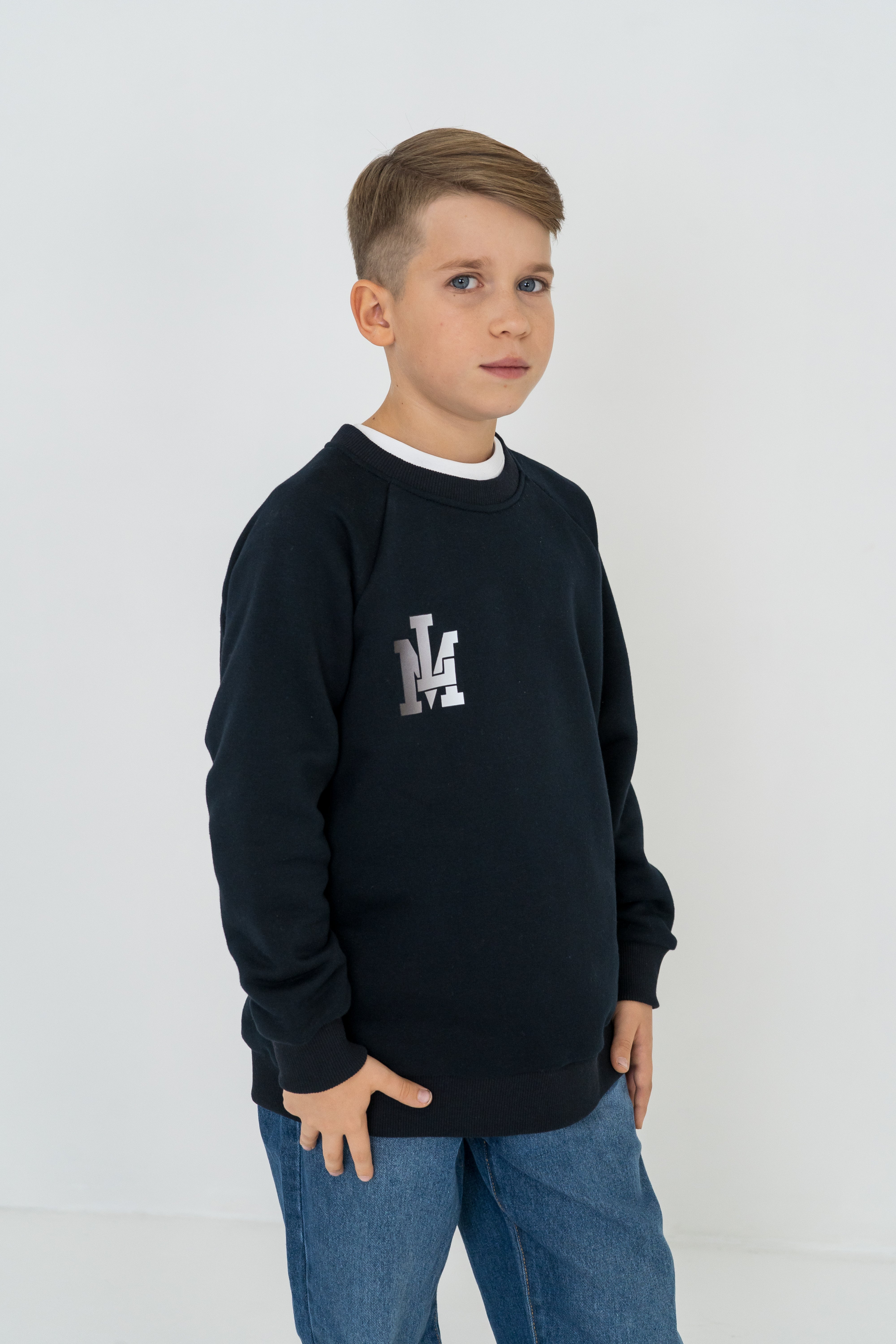 Junge trägt das dunkelblaue Langarmshirt mit dem kleinen Print LM in Kombination mit Jeans.