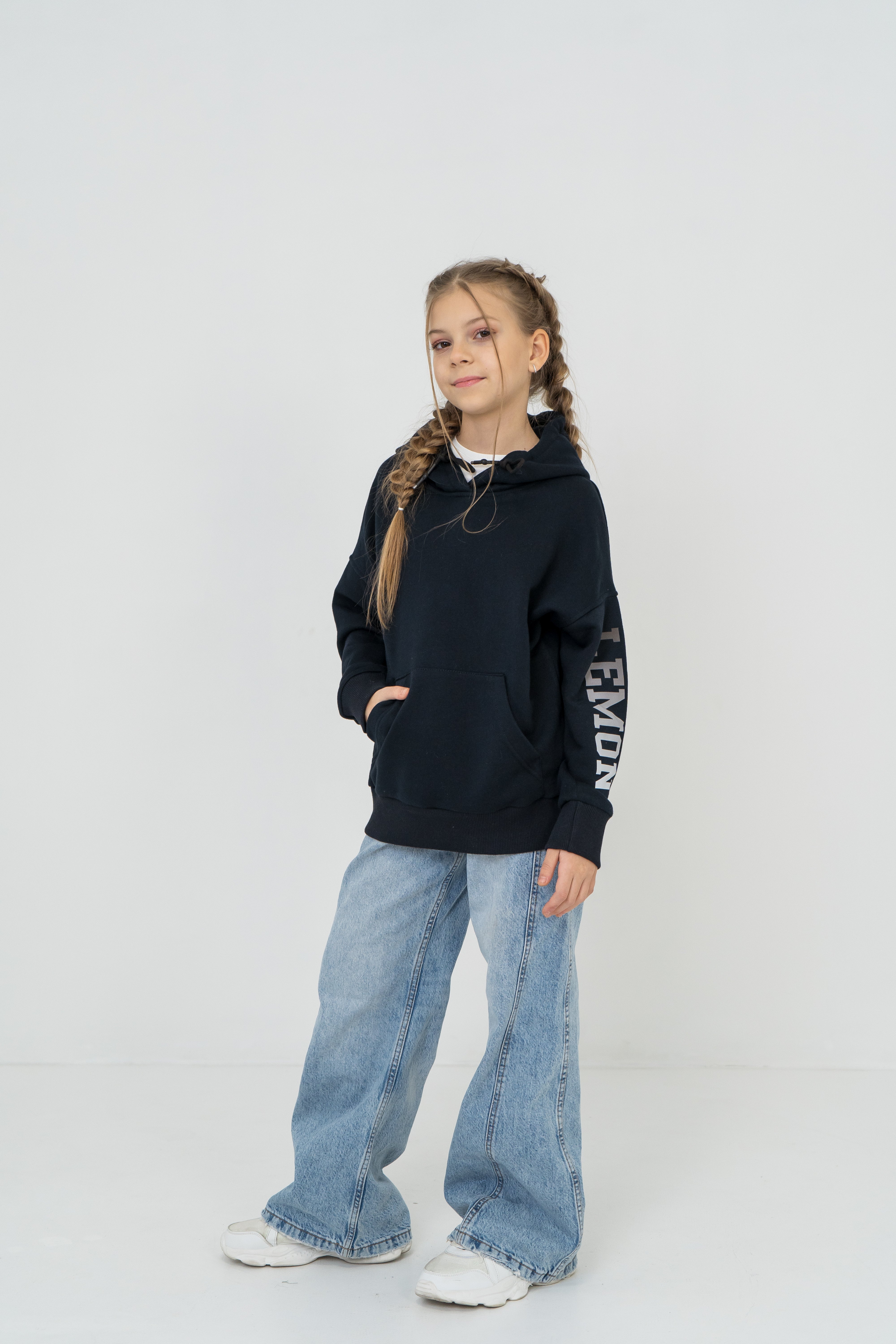 Mädchen trägt den dunkelblauen Pullover mit dem Lemoni Print am Ärmel, kombiniert mit Jeans