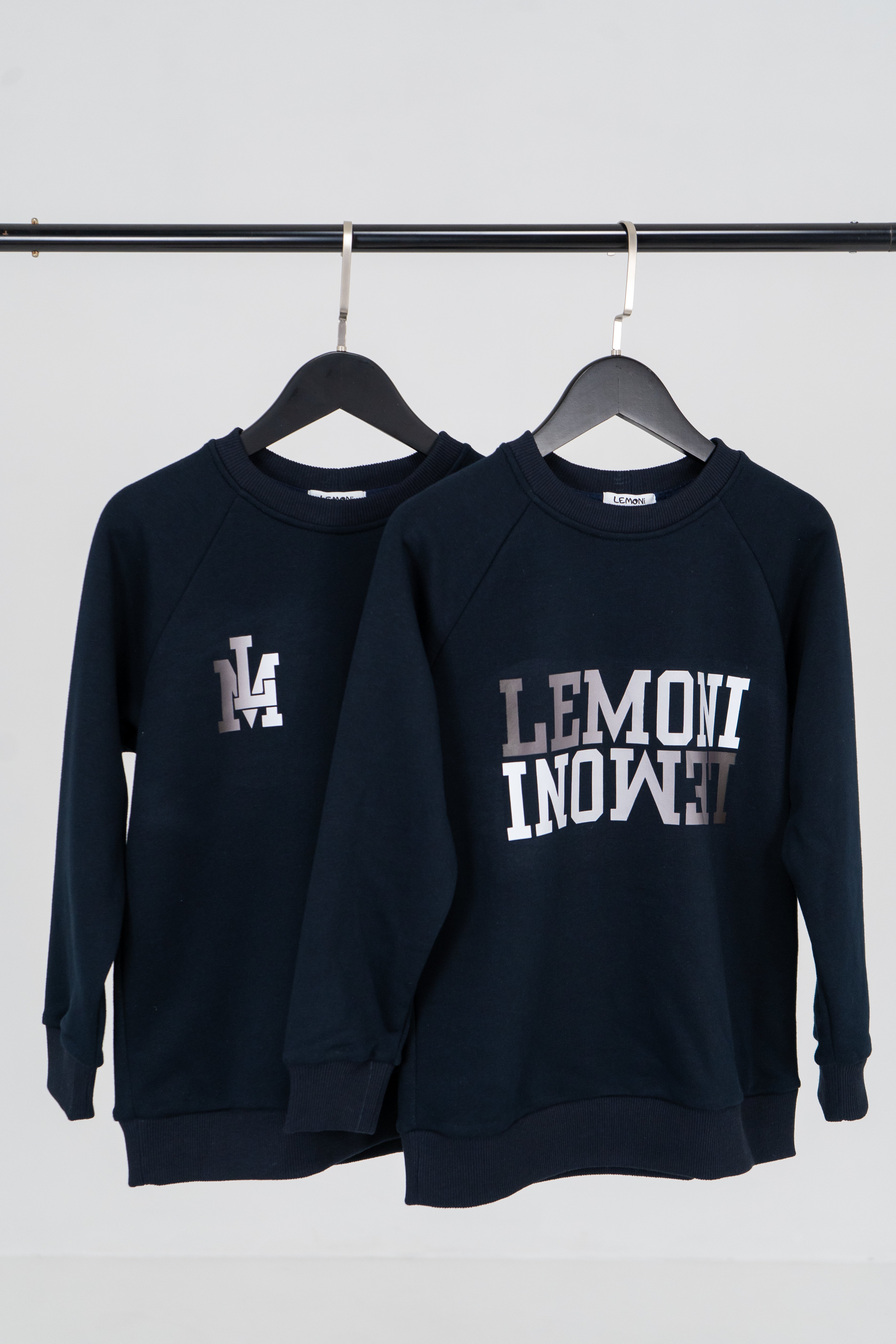 Zwei dunkelblaue Sweatshirts von Lemoni mit kleinem und größeren Print hängen auf den Bügeln.