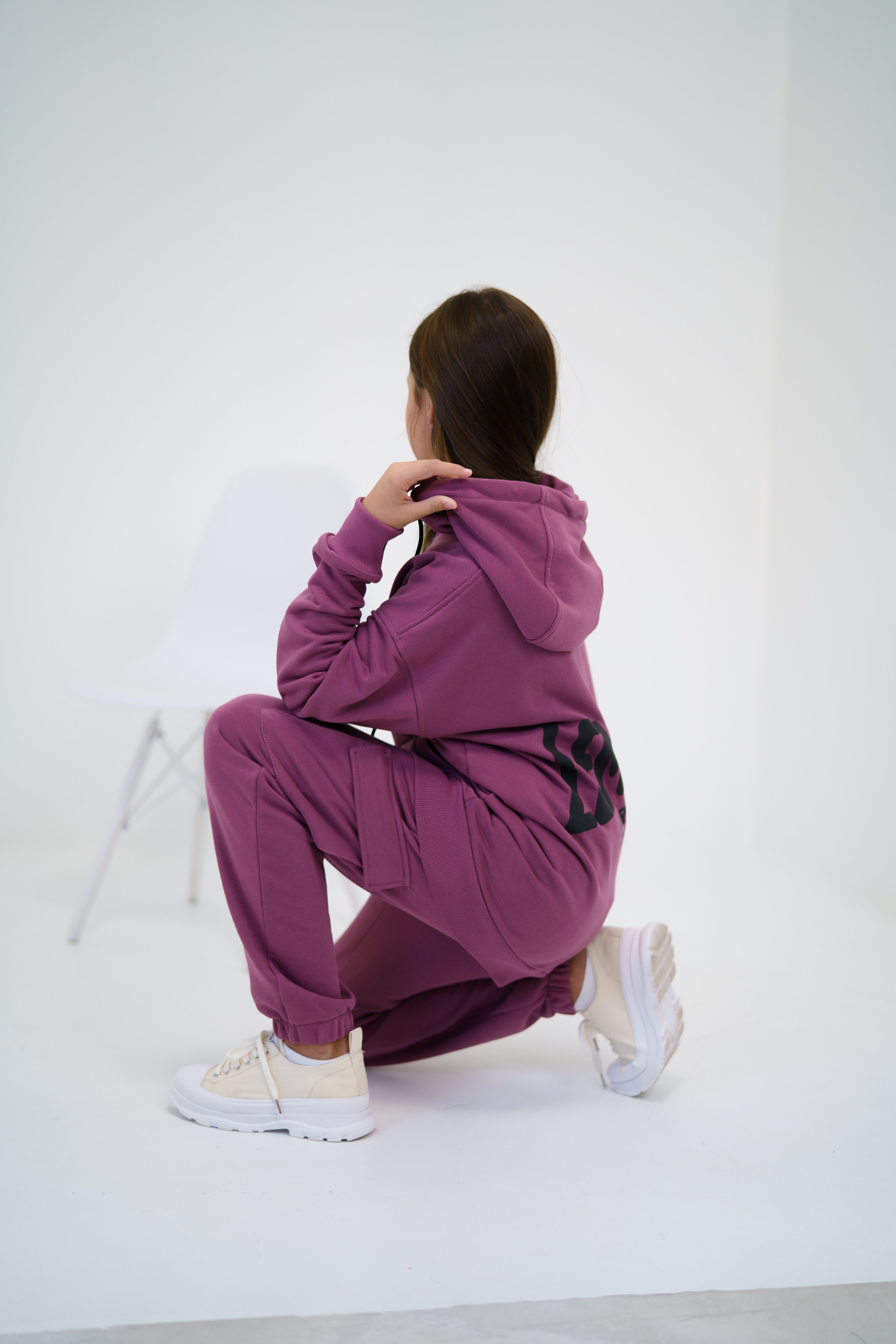 girl in a pink tracksuit by Lemoni is sitting on the ground - side view