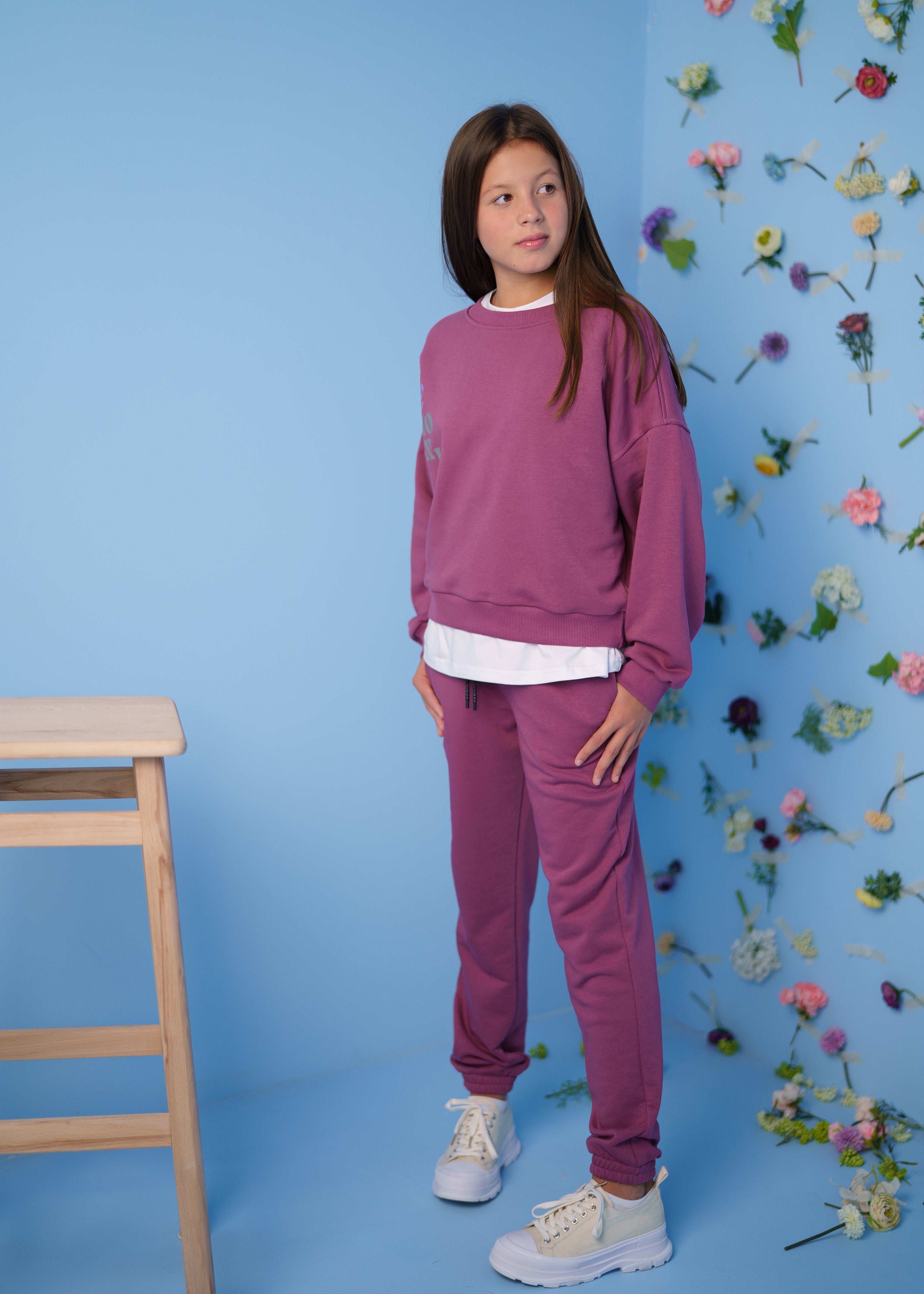 girl wearing a pink tracksuit with a sweatshirt by Lemoni with a flower wall on the background